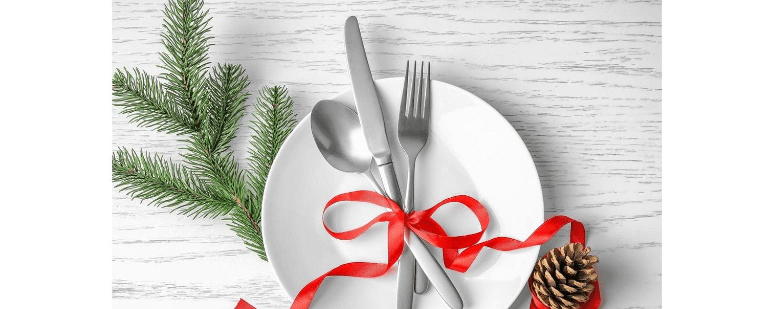Utensils tied with ribbon on plate, next to conifer sprig