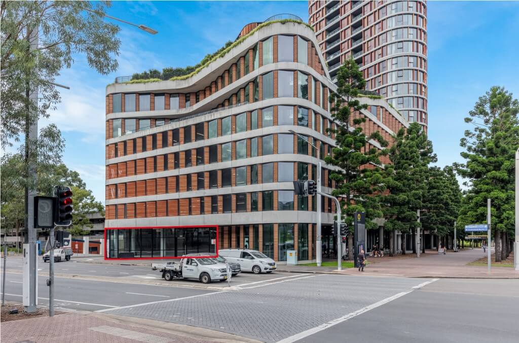 Modern curved building on a street corner with glass-front retail space on the ground floor.