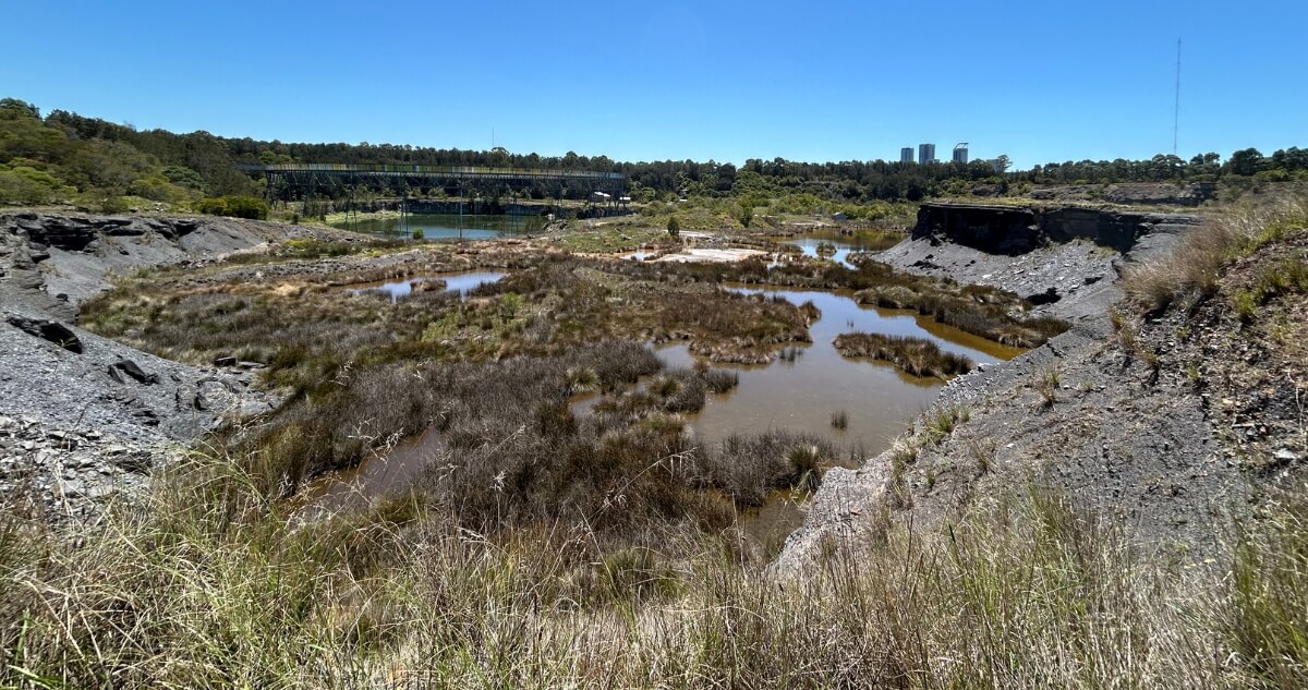 A series of shallow, vegetation‑filled freshwater wetland pools sit within a rocky, eroded landscape under a clear blue sky.